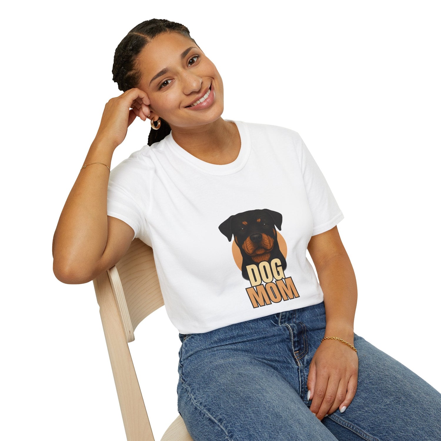 A lady sits in a chair resting her head on a her closed hand smiling at the camera wearing a white T-shirt that days Dog Mom on it and has a picture of a Rottwieleer